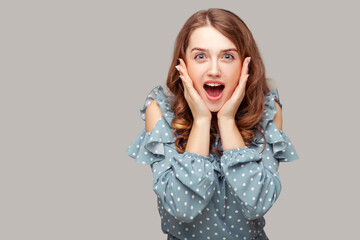 Oh my god, wow! Surprised excited brunette girl ruffle blouse touching face looking at camera amazed, open mouth in astonishment, shocked by unbelievable news. studio shot isolated on gray background