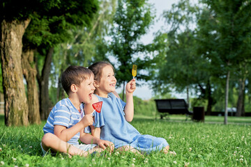 two children with lollipops sit on the green grass in summer