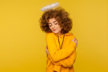 I love myself! Portrait of curly-haired beautiful angelic woman with saint nimbus embracing herself...