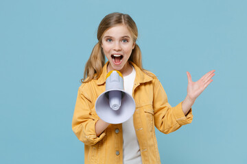 Shocked little blonde kid girl 12-13 years old in yellow jacket posing isolated on pastel blue wall background. Childhood lifestyle concept. Mock up copy space. Screaming in megaphone spreading hands.