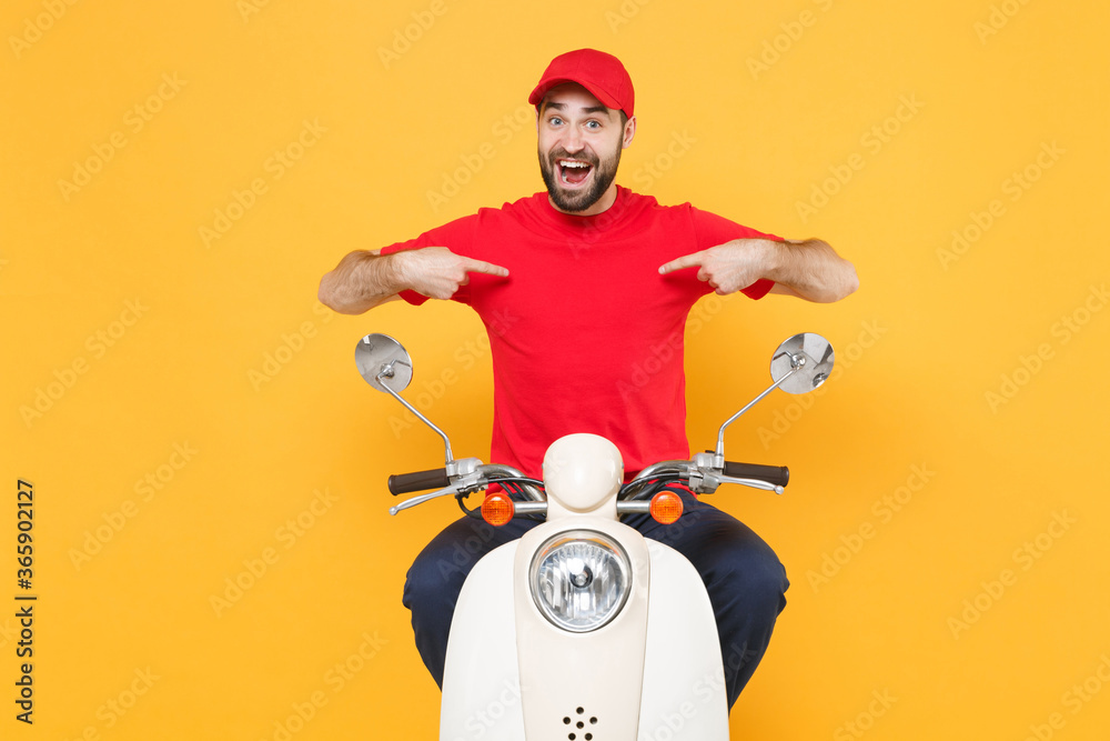 Wall mural Delivery man in red cap t-shirt uniform driving moped motorbike scooter isolated on yellow background studio Guy employee working courier Service quarantine pandemic coronavirus virus covid-19 concept