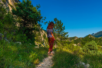 A full body shot of an unrecognizable young Caucasian redhead hiker standing on a hiking footpath path in the French Alps during sunset