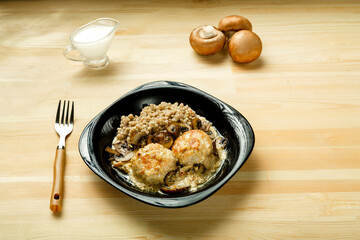 Chicken meatballs with champignons in a creamy sauce with a side dish of green buckwheat near a fork mushrooms and cream.