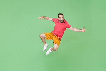 Fototapeta na wymiar Excited young bearded man guy in casual red pink t-shirt posing isolated on green background studio portrait. People sincere emotions lifestyle concept. Mock up copy space. Jumping spreading hands.