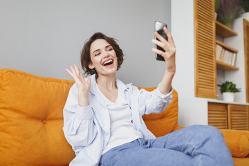 Funny girl in casual clothes sitting on couch spending time in living room at home. Rest relax good...