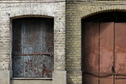 Rusted metal door and closed window shutter on the abandoned building facade.