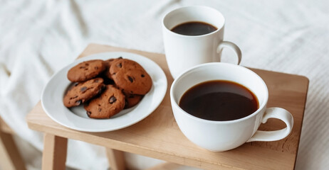 Breakfast in bed. Hot coffee with oatmeal cookies with chocolate on a wooden tray.