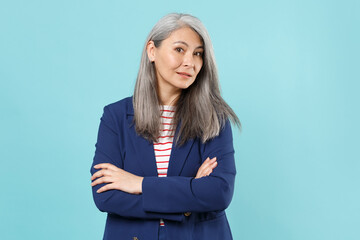 Successful gray-haired business woman in blue suit posing isolated on pastel blue background studio portrait. Achievement career wealth business concept. Mock up copy space. Holding hands crossed.