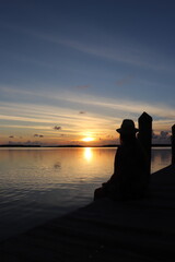 silhouette of a woman sitting on a pier at sunset