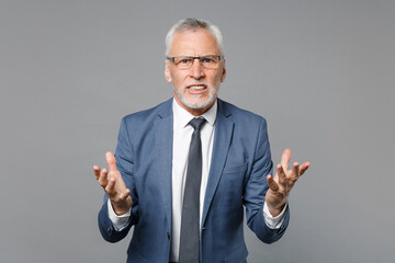 Irritated elderly gray-haired mustache bearded business man in classic blue suit shirt tie isolated on grey background studio. Achievement career wealth business concept. Spreading hands swearing.