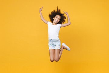 Fototapeta na wymiar Full length portrait of funny little african american kid girl 12-13 years old in white t-shirt isolated on yellow wall background. Childhood lifestyle concept. Jumping, pointing index fingers up.