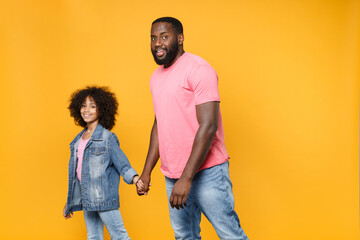Obraz premium Smiling african american guy girl brother sister in denim pink clothes isolated on yellow wall background studio portrait. People lifestyle concept. Mock up copy space. Holding hands, walking going.