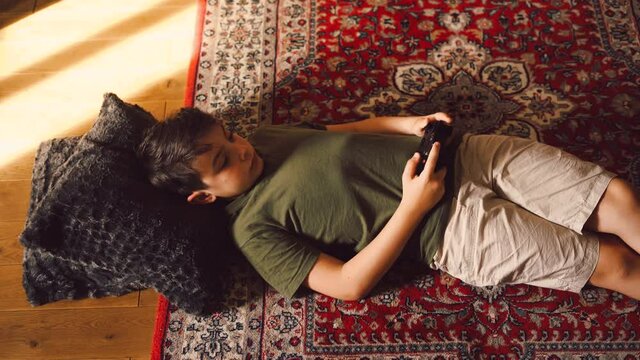 Cute child lying on carpet at home and playing on console