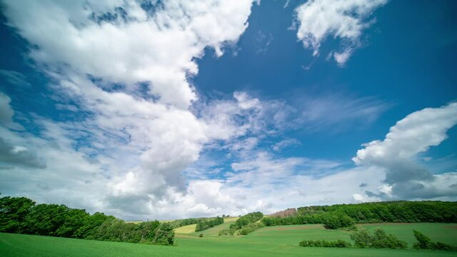 White clouds on blue sky over green field of days time lapse