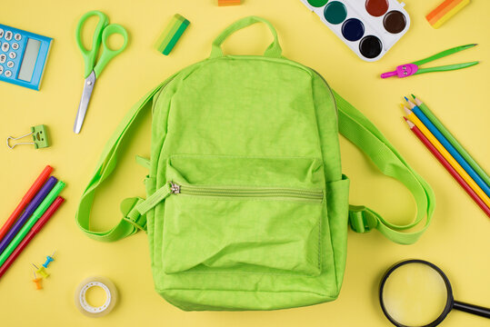 Back to school concept. Top above overhead view photo of green backpack and colorful stationery isolated on yellow background