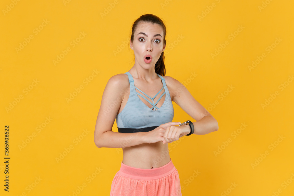 Wall mural Shocked young fitness sporty woman girl in sportswear working out isolated on yellow background studio. Workout sport motivation lifestyle concept. Mock up copy space. Wearing smart watch on hand.