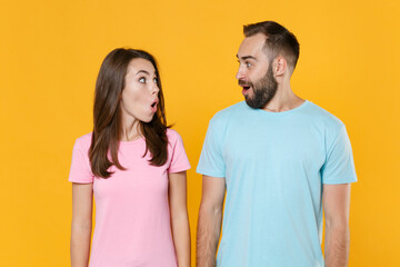 Fototapeta premium Amazed young couple two friends guy girl in blue pink t-shirts posing isolated on yellow background studio. People lifestyle concept. Mock up copy space. Keeping mouth open, looking at each other.