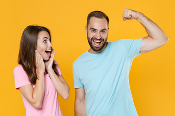 Excited young couple friends guy girl in blue pink t-shirts isolated on yellow background studio portrait. People lifestyle concept. Mock up copy space. Showing biceps, muscles, put hands on cheeks.