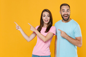 Surprised young couple two friends guy girl in blue pink t-shirts isolated on yellow background...
