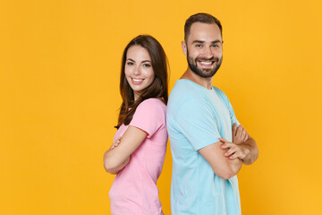 Naklejka premium Side view of smiling couple friends guy girl in blue pink t-shirts isolated on yellow background. People lifestyle concept. Mock up copy space. Standing back to back hold hands crossed looking camera.