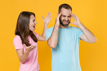 Dissatisfied young couple friends guy girl in blue pink t-shirts posing isolated on yellow background studio portrait. People lifestyle concept. Mock up copy space. Screaming swearing spreading hands.
