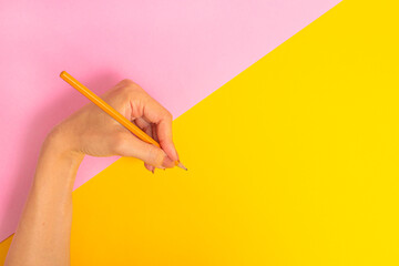 The left hand is holding a pencil and is about to write something on a bright pink-yellow...
