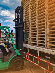 Worker driving forklift to loading and unloading wooden pallets from truck to warehouse cargo storage, shipment in logistics and transportation industrial, wood pallets stack