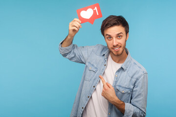 Click Like! Portrait of cheerful handsome blogger man in denim shirt pointing at social media heart Like button, emoji counter, follower notification. indoor studio shot isolated on blue background