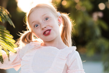 Blonde child girl 4-5 year old having fun outdoors over sunny background closeup. Childhood. Looking at camera.