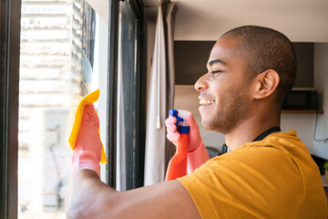 Male housekeeper cleaning glass window at home.