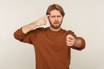 You are idiot! Portrait of bearded man showing stupid gesture, pointing finger to camera and...