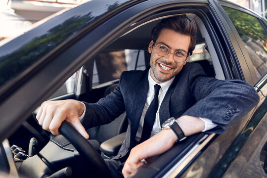 Happy Young Man In Full Suit And Eyewear Smiling While Driving A Car