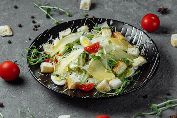 Fresh Caesar salad in a black plate on a gray background.Top view