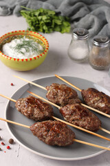 Kofta kebab on wooden skewers on a plate and sauce on the table, traditional dish of Arab cuisine, grilled minced meat shish kebab