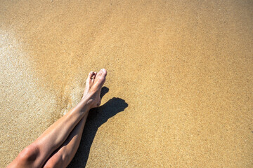 Long slim young woman legs relaxing lying down and sunbathing on sand tropical beach under hot sun...