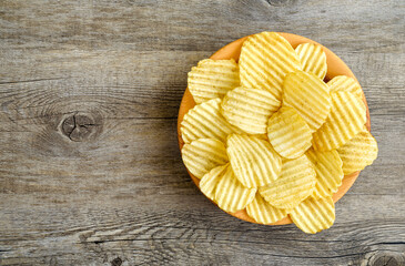 Corrugated golden potato chips in a wooden bowl on rustic wooden table. Top view with Empty space for text.