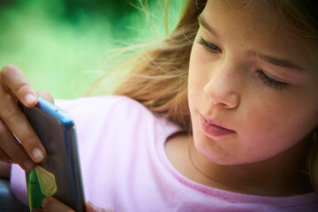 Child girl playing on smartphone playing games outdoors during summer day