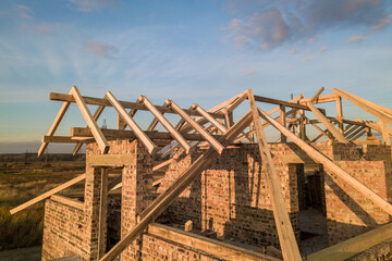 Private residential house with wooden roof frame structure under construction. Unfinished brick building under development.