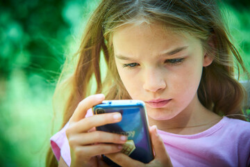 Child girl playing on smartphone playing games outdoors during summer day