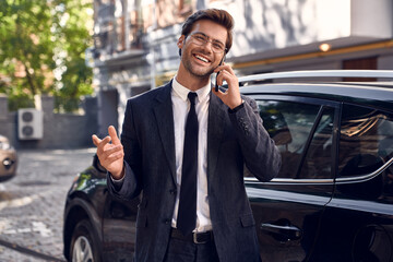 Confident business expert. Full length of handsome young businessman talking on the phone while standing near his car outdoors