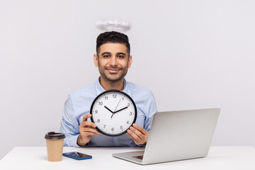 Time management. Positive punctual man employee with angelic nimbus sitting in office workplace,...