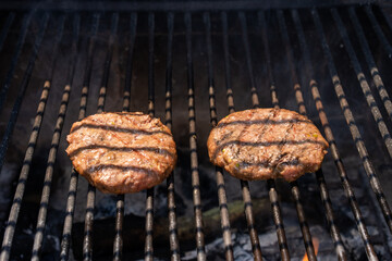 Hamburguesas cocinándose en una barbacoa de carbón bajo la luz del sol