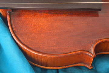 Ein Teil von einem Geigen Korpus, von  dem Griffbrett des Instruments und von einer Seite was auf einem Seidenen blauen Tuch liegt. . Die Maserung des Holzes hat braun-rote Töne
