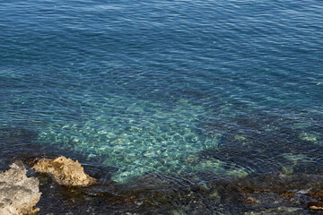 Fototapeta na wymiar Turquoise surface of waving water in sunshine on tropical rocky beach in Crete, Greece. Copy space.