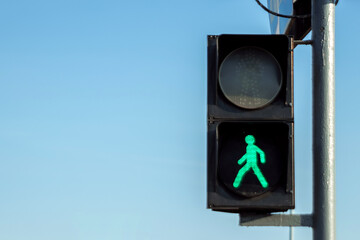green pedestrian traffic light against the sky.