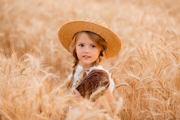 A little blonde girl holds a fresh loaf of bread in a wheat field in the summer. Eco-friendly farm products