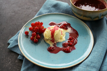 Vanilla ice cream with red currants and fruit jelly sauce on a blue plate, napkin and dark background with copy space