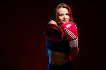 The girl athlete professional boxer in red gloves make an impact in the direction of the camera. A professional athlete during exercise.