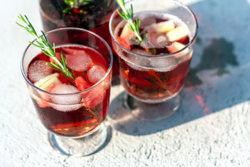 Two glasses and carafe with red refreshing summer drink or red wine, ice cube, pieces of watermelon and rosemary sprigs. Summertime concept. Selective focus.