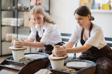 Overview of two young potters by pottery wheels while preparing ceramic pots from raw clay.